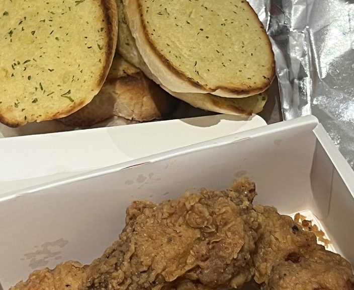 Foil-wrapped garlic bread halves above a box of fried chicken